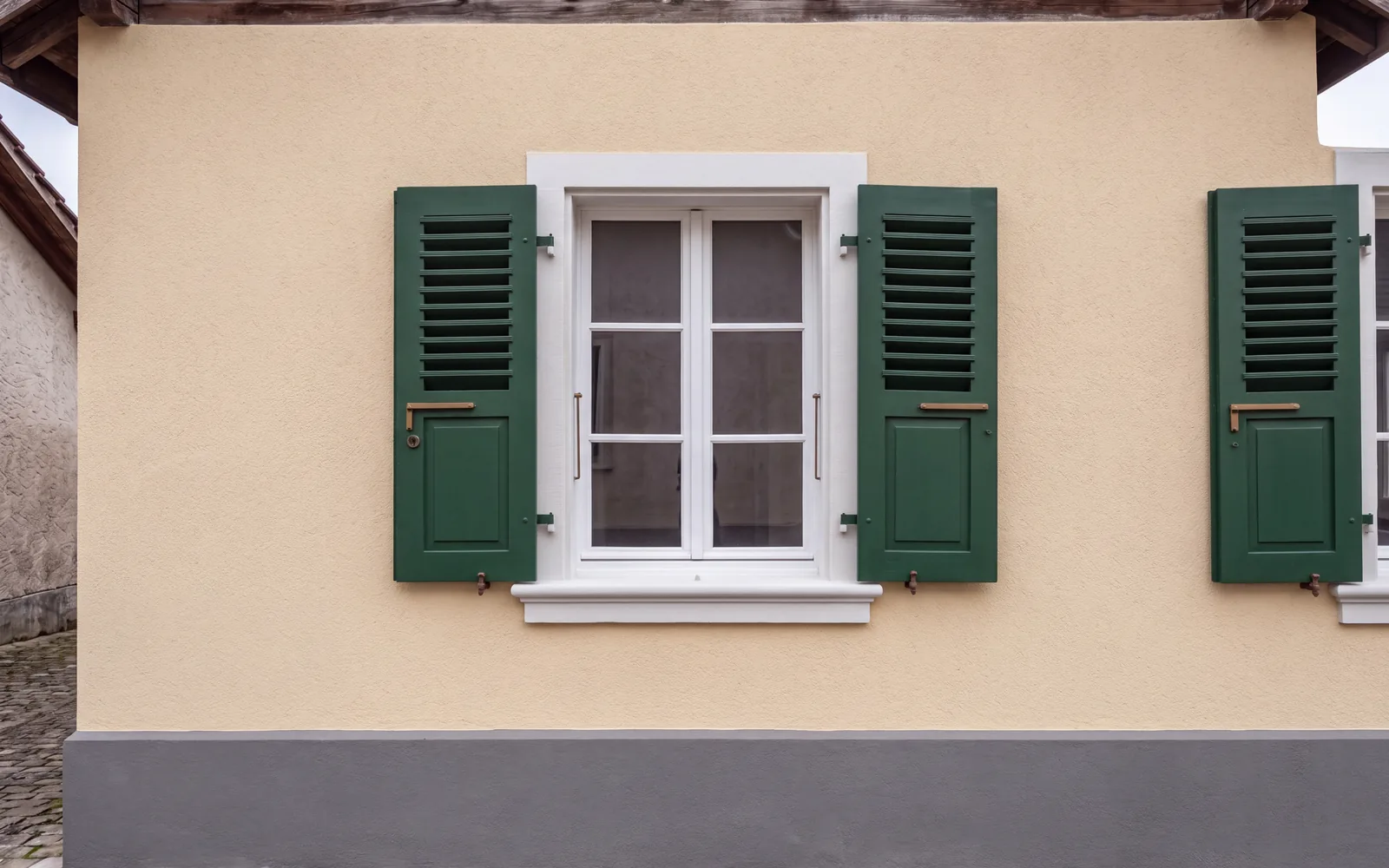 La façade après rénovation : crépi neuf couleur crème, volets repeints en vert foncé, soubassement anthracite